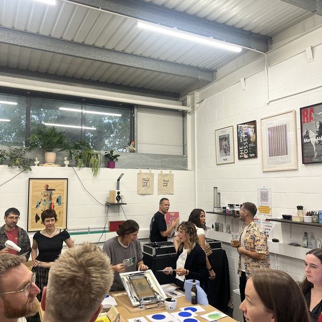 A group gathered around the print table during a workshop evening at flood and pull.