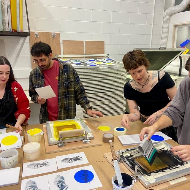 Four workshop guests printing together at the bench, inks and screens laid out in front of them.