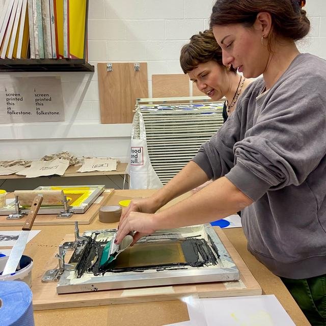 Two people working closely together to coat and prepare a screen.